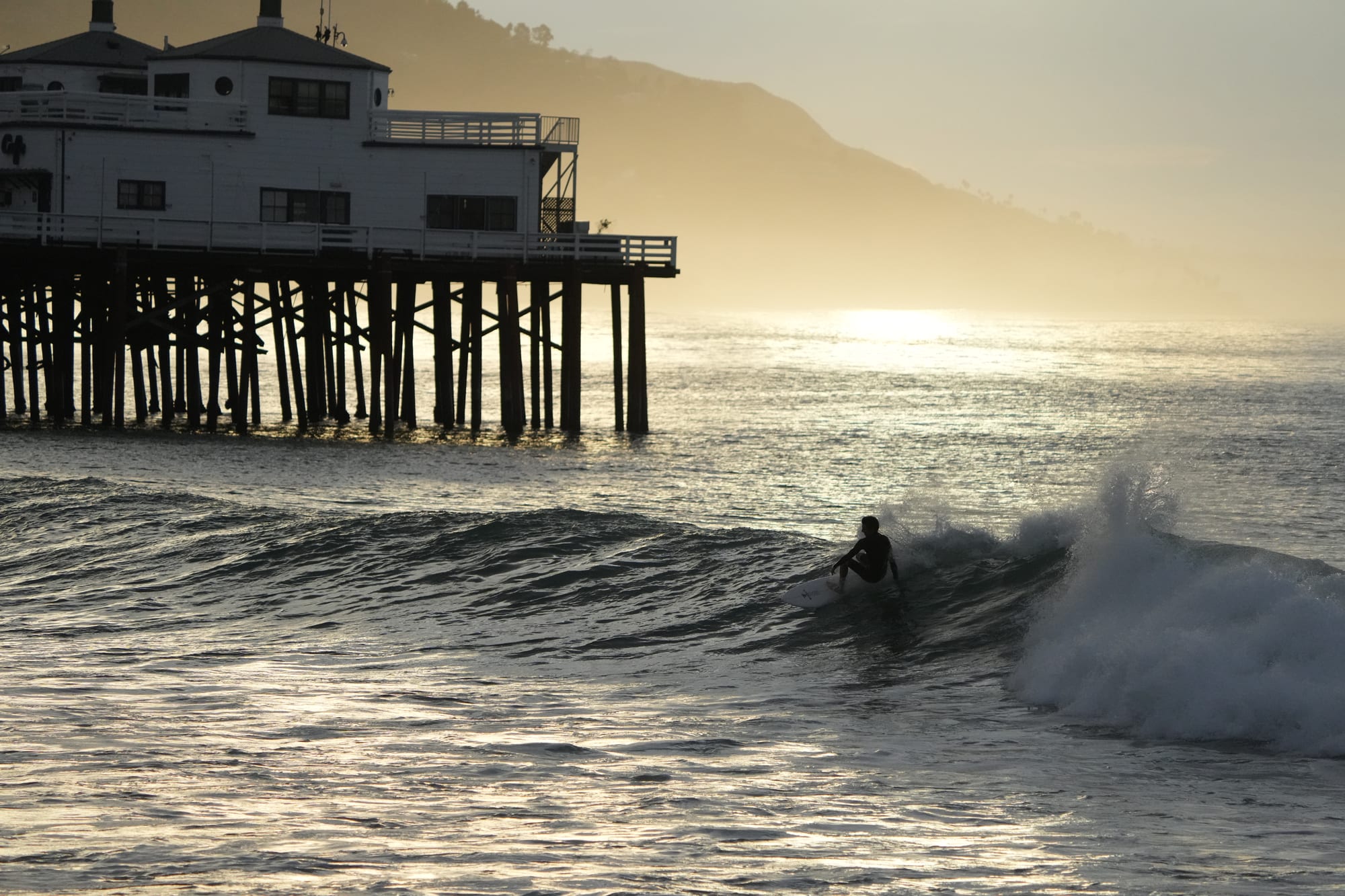 Surfer under the pier at sunset