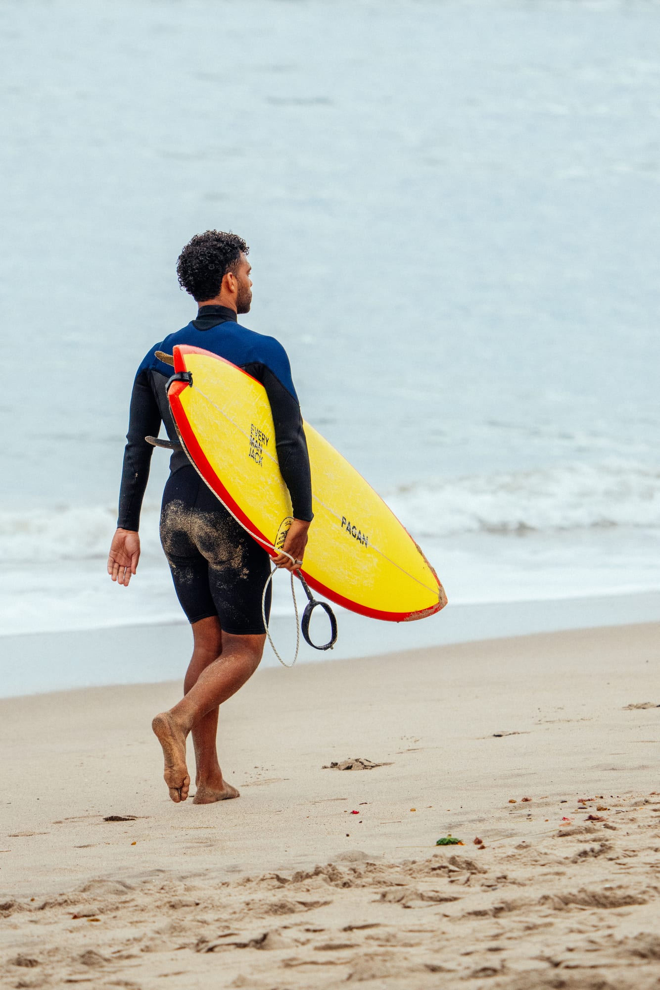Surfer walking up the beach with a yellow board